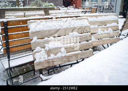 Schnee fällt auf Holztischen und -Stühlen in einem Biergarten im Winter Stockfoto