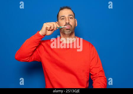 Bärtiger hispanischer Mann in seinen 40ern putzte seine Zähne mit einer Zahnbürste und Zahnpasta, putzte Zähne und Zunge als gesunde Morgen-Gesundheitspflege Stockfoto
