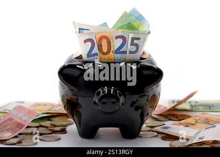 Bargeld in voller Schweinebank zeigen das Jahr 2025, Euro-Banknoten mit Münzen liegen neben der Geldbox und symbolisieren das Sparen oder Anlegen von Geld im neuen Jahr Stockfoto