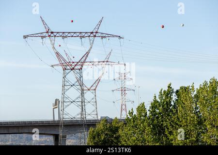 Strommasten und Stromleitungen dominieren die Skyline, überqueren eine Brücke und erstrecken sich über eine ländliche Landschaft Stockfoto