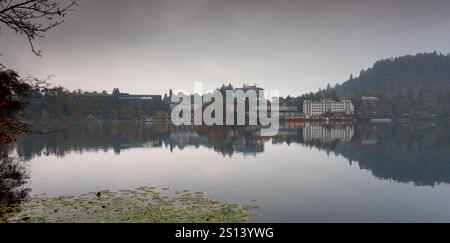 Ruhiges Wasser reflektiert Hotels und Bäume am Ufer des Sees Bled in slowenien an einem nebeligen Herbsttag Stockfoto