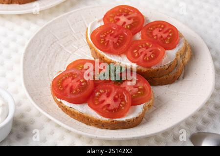 Köstliche Sandwiches mit offenem Gesicht, belegt mit frischen Tomaten und Frischkäse, serviert auf einem strukturierten weißen Teller Stockfoto