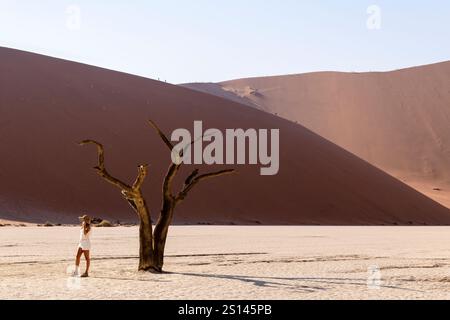SESRIEM, NAMIBIA - 21. AUGUST 2024: Weibliche Touristin mit Sonnenhut vor Dead Tree and Dune Stockfoto