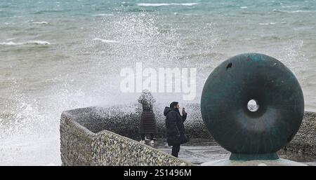 Brighton UK 31. Dezember 2024 - Wanderer werden nass, wenn Wellen an einem windigen Tag auf Brightons Küste krachen, da stürmisches Wetter viele Silvesterfeuerwerke im ganzen Land abgesagt hat: Credit Simon Dack / Alamy Live News Stockfoto