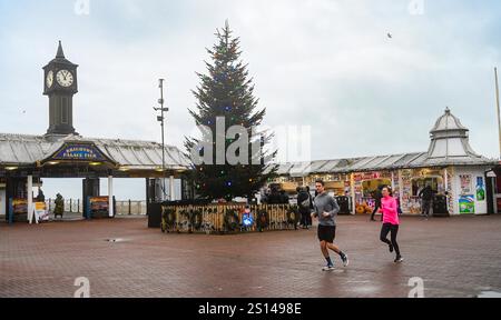 Brighton UK 31. Dezember 2024 - Läufer, die dem Wind trotzen, passieren den Weihnachtsbaum am Brighton Palace Pier, da stürmisches Wetter dazu geführt hat, dass viele Silvesterfeuerwerke im ganzen Land abgesagt wurden: Credit Simon Dack / Alamy Live News Stockfoto