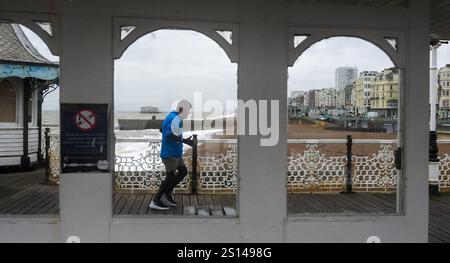 Brighton UK 31. Dezember 2024 - Ein Läufer trotzt dem Wind am Brighton Palace Pier, da stürmisches Wetter dazu geführt hat, dass viele Silvesterfeuerwerke im ganzen Land abgesagt wurden: Credit Simon Dack / Alamy Live News Stockfoto