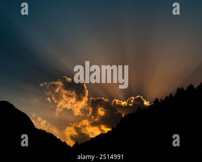Sonnenstrahlen, die hinter der Wolke leuchten. Sonnenuntergang mit mountail Silhouetten. Stockfoto