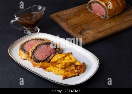 Rindfleisch Wellington mit gebackener Kartoffelscheibe und Demi-Glace-Sauce. Traditionelles festliches Gericht aus Rinderfilet mit Pilzen und Parmaschinken, gebacken in Blätterteig Stockfoto