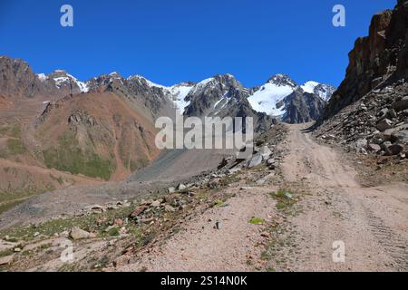 Atemberaubende Berggipfel, bedeckt mit Gletschern, Landstraße und klarem blauem Himmel über den zentralen Tian-Shan-Bergen in der Nähe von Almaty in Kasachstan. Am Besten Stockfoto