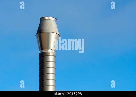 Dieses Foto zeigt eine glänzende Schornsteinkappe aus Metall, die sich gegen einen riesigen klaren blauen Himmel erhebt. Die Kappe ist zylindrisch und zeigt ein modernes Design mit glattem Design Stockfoto