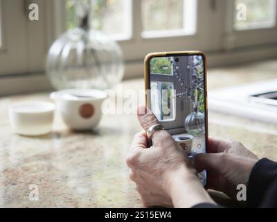 Nahaufnahme, weibliche Hände halten Smartphone und machen ein Foto von einer Tasse auf der Küchenarbeitsplatte. Unscharfer Hintergrund Stockfoto