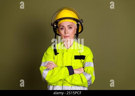 Reife Feuerwehrfrau in gut sichtbarer Arbeitskleidung und Helm vor khakifarbenem Hintergrund Stockfoto