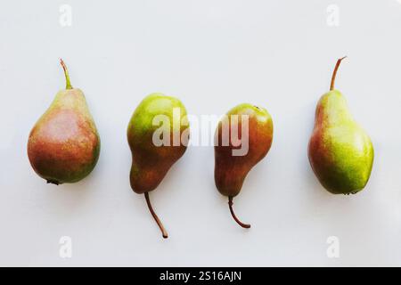 Vier schöne, appetitliche rot-grüne Birnen liegen auf einem hellen Hintergrund, Blick von oben. Das Konzept frischer Früchte, Vitamine. Stockfoto