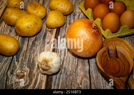 Kartoffeln, Eier, eine Zwiebel, ein Knoblauch und ein Holzlöffel auf einem Holztisch Stockfoto