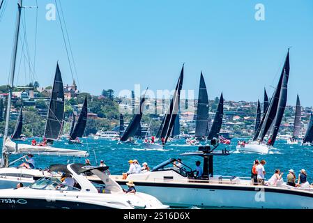 Von einer langen Reihe von Zuschauerbooten bewacht, drängen sich Yachten aller Größen vor dem Start des Yachtrennens von Sydney nach Hobart 2024 um Positionen Stockfoto