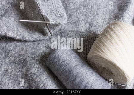 Grau melierter Strickpullover mit Stricknadeln. Mischung aus grauer Wolle und weißem Kaschmir mit Nadeln. Hintergrund des Strickmusters. Strick Lifestyle Stockfoto