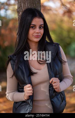 Die modische junge Frau posiert im Herbstpark und genießt warmes Wetter und buntes Laub Stockfoto