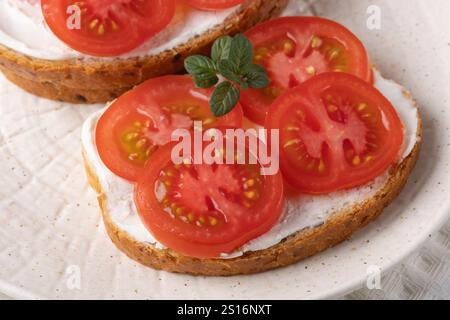 Köstliche Sandwiches mit offenem Gesicht, belegt mit frischen Tomaten und Frischkäse, serviert auf einem strukturierten weißen Teller Stockfoto