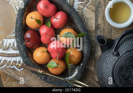 Blick von oben auf Deletable Imitation Fruits (Kanom Look Choup) hat einen süßen Geschmack serviert mit heißem Tee auf hölzernem Schneidebrett. Traditionelle thailändische Süßigkeiten Stockfoto