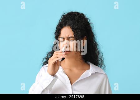 Junge afroamerikanische Frau mit Nasenspray auf blauem Hintergrund. Allergiekonzept Stockfoto