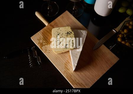 Köstliche Gourmet-Käsesorten auf einem Holzbrett mit Gläsern Wein und Vorspeisen. Stockfoto
