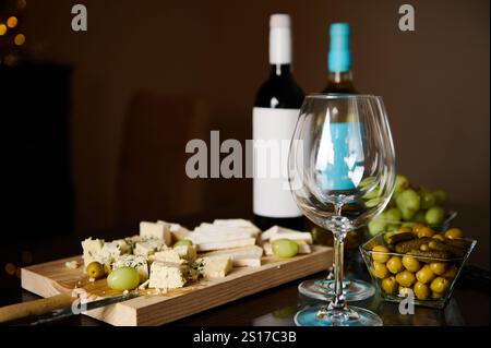 Ein raffiniertes Arrangement aus Weinflaschen, Gläsern, Käseplatten, Trauben und grünen Oliven auf einem dunklen Tisch in ruhiger Atmosphäre. Perfekt für Gat Stockfoto
