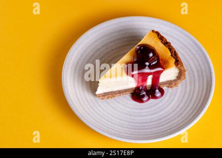 Eine in Scheiben geschnittene Portion eines tiefgefüllten New Yorker Käsekuchens mit schwarzen Kirschen. Der Kuchen wird auf Teller serviert. Stockfoto