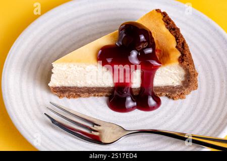 Eine in Scheiben geschnittene Portion eines tiefgefüllten New Yorker Käsekuchens mit schwarzen Kirschen. Der Kuchen wird auf Teller serviert. Stockfoto