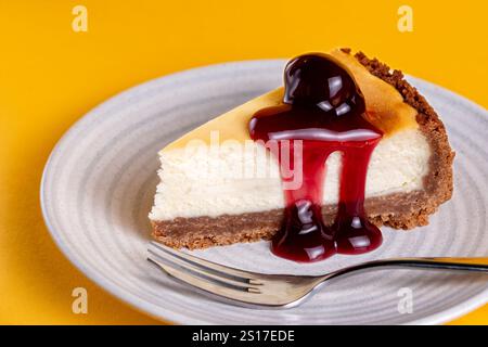 Eine in Scheiben geschnittene Portion eines tiefgefüllten New Yorker Käsekuchens mit schwarzen Kirschen. Der Kuchen wird auf Teller serviert. Stockfoto