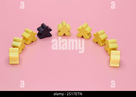 Holzfiguren in gelber und schwarzer menschlicher Form auf rosafarbenem Hintergrund. Stockfoto