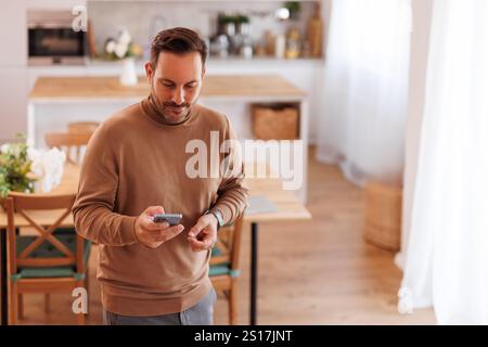 Hochwinkelansicht eines selbstbewussten Geschäftsmannes im mittleren Erwachsenenalter, der in der Küche über das Smartphone SMS sendet Stockfoto