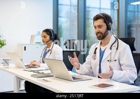 Zwei Ärzte, die Patienten aus der Ferne konsultieren, Mann und Frau mit Headset mit Laptop für Videoanrufe, arbeiten in der Klinik, Patientenbetreuung und Assistenzdienst. Stockfoto
