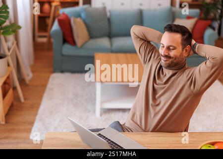 Hochwinkelansicht eines glücklichen Geschäftsmannes mit geschlossenen Augen und Händen hinter dem Kopf, die sich am Schreibtisch im Heimbüro entspannen Stockfoto