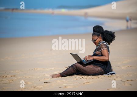 Frau, die am Strand an ihrem Laptop arbeitet Stockfoto