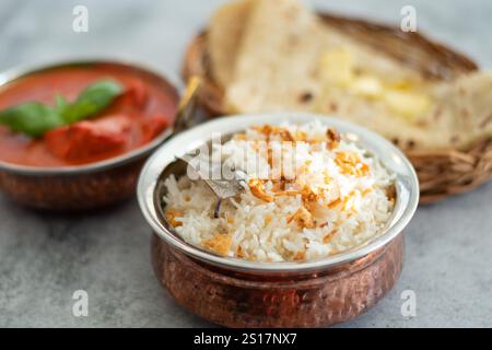 Rauchiger weißer Reis. Zubereitet und in einer Messingschale serviert. Naturholz im Hintergrund. Gebratener Reis in einer Schüssel mit Beilage auf schwarzem Hintergrund. Copysp Stockfoto