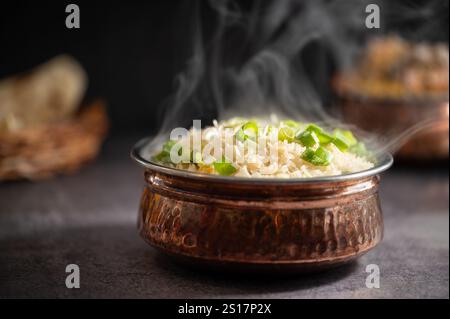 Rauchiger weißer Reis. Zubereitet und in einer Messingschale serviert. Naturholz im Hintergrund. Gebratener Reis in einer Schüssel mit Beilage auf schwarzem Hintergrund. Copysp Stockfoto
