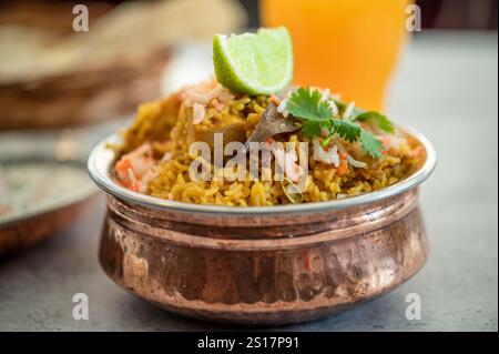 Würziger indischer Biryani-Pulao in goldener Schüssel mit indischem Basmati-Reisgericht mit Hühnerfleisch-Curry Ramadan Kareem, Eid. Servierschale aus Messing mit weißem Rücken Stockfoto