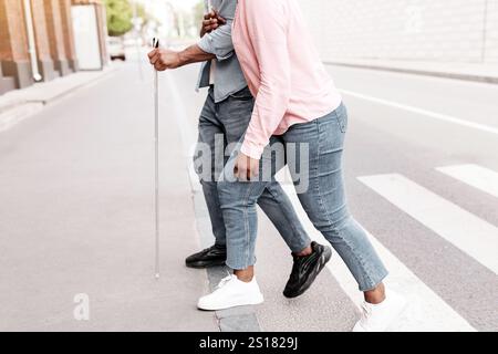 Nicht erkennbare junge schwarze Frau, die Millennials mit Sehbehinderung dabei unterstützt, die Straße der Stadt zu überqueren und den Raum zu kopieren Stockfoto