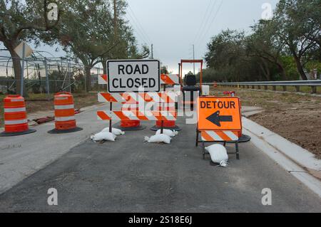 Weitsicht Schwarzes und weißes Straßenschild mit geschlossenem Schild und orangefarbenem Umleitungsschild. Wasserreparatur auf einer großen Baustelle. Orangenkegel und Fass mit Leadi Stockfoto