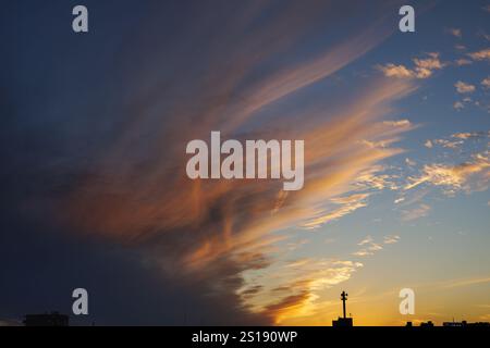 Feurige orangene Wolken erstrecken sich in der Abenddämmerung von einer dunklen Wolkenbank nach oben und fassen die letzten Spuren des klaren blauen Himmels, bevor die Sonne untergeht. Stockfoto