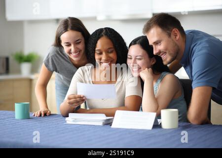 Vier glückliche Mitbewohner, die in der Küche zu Hause den Kontoauszug überprüfen Stockfoto