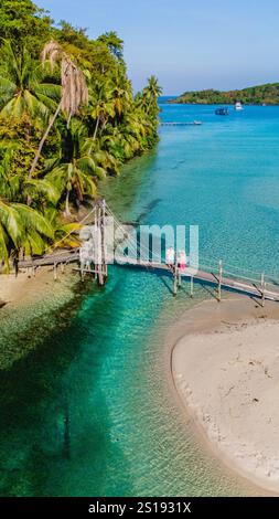 Inmitten der üppigen Palmen verbindet eine Holzbrücke zwei bezaubernde Punkte entlang der Küste von Koh Kood. Das türkisfarbene Wasser glitzert unter dem hellblauen Himmel und lädt Reisende ein, die Stadt zu erkunden. Stockfoto