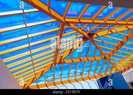 Moderne architektonische Struktur mit Holzgerüst und Glasdach. Lebendiger Himmel, sichtbar durch Glaspaneele und kompliziertes Design aus Holz-BE Stockfoto