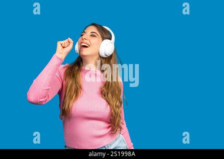 Unbeschwerte junge Frau, die mit kabellosen Kopfhörern zu ihrem Lieblingslied singt und einen Moment purer musikalischer Glückseligkeit genießt Stockfoto