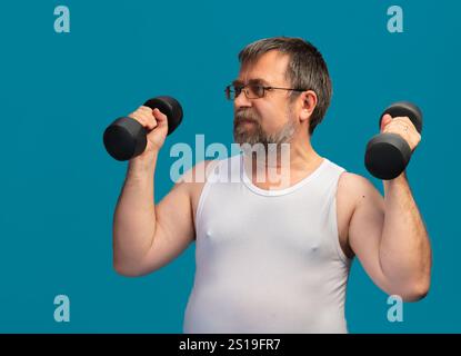 Ein älterer Mann trainiert, indem er Hanteln hebt, um seine Kraft zu erhöhen. Er konzentriert sich auf sein Workout, während er ein ärmelloses Hemd trägt. Das helle B Stockfoto