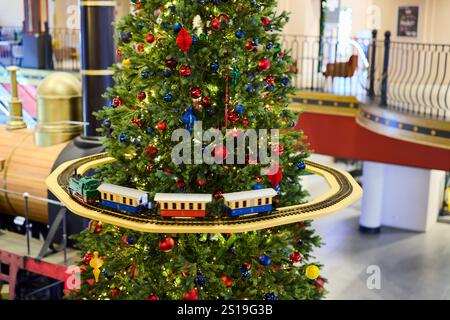 Ein wunderschöner und festlicher Weihnachtsbaum mit einer bezaubernden Zugausstellung darunter Stockfoto