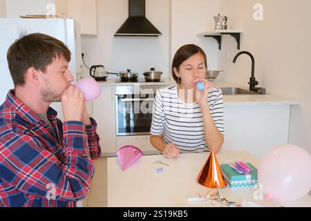 Das junge Paar feiert zu Hause gemütlich Geburtstag und genießt Kuchen und Lachen in warmer Atmosphäre. Fröhliche Atmosphäre, farbenfrohe Dekoration, Vorbereitung auf holi Stockfoto