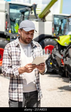 Vertikales Foto eines männlichen Arbeiters mit digitalem Tablet im Landmaschinenbetrieb. Stockfoto