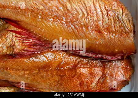 Heiß geräucherter Barsch Fisch in weißer Plastikverpackung auf hölzernem Hintergrund. Nahaufnahme, Draufsicht Stockfoto