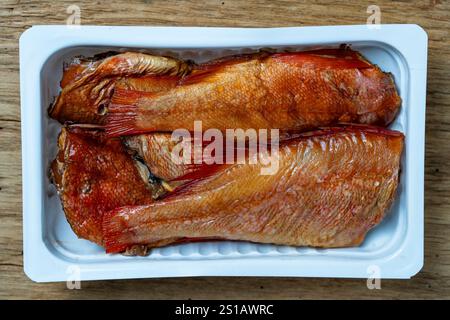 Heiß geräucherter Barsch Fisch in weißer Plastikverpackung auf hölzernem Hintergrund. Nahaufnahme, Draufsicht Stockfoto